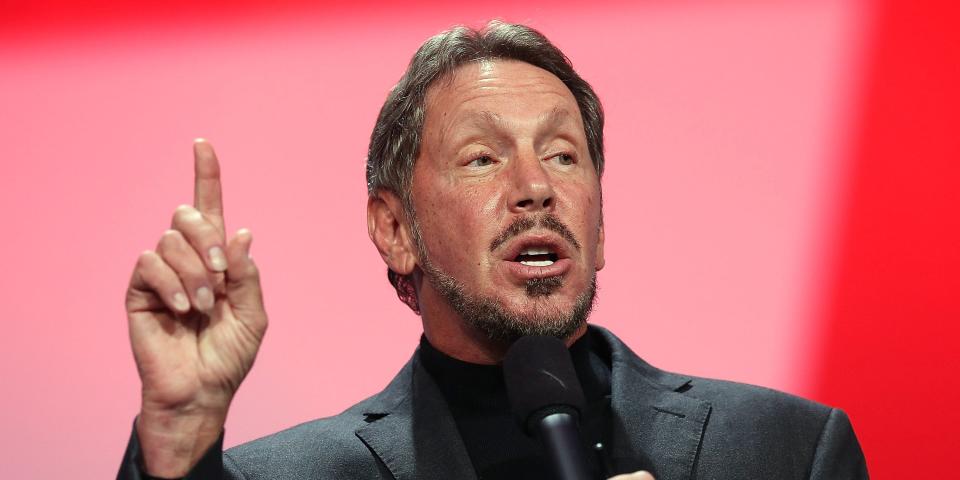 拉里·埃里森 (Larry Ellison) 对着麦克风讲话,手指向上。