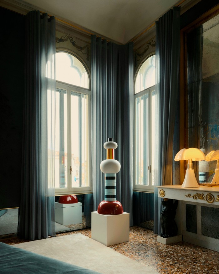 两扇大的拱形窗户挂着透明的蓝色窗帘,位于条纹和球状图腾的两侧。房间有橙色、奶油色和蓝色水磨石地板和镜面墙板